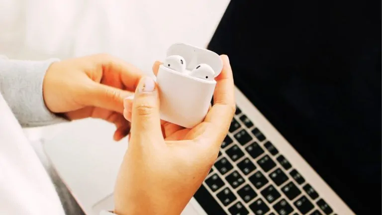 A person holding an open AirPods case near a laptop. For a smooth connection, follow the steps for how to connect AirPods to a laptop.